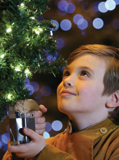 Lighting of the tree blessing of the crib service at Liverpool Cathedral - young chorister carry one of the lighted trees, christmas lights in the background. © Gareth Jones