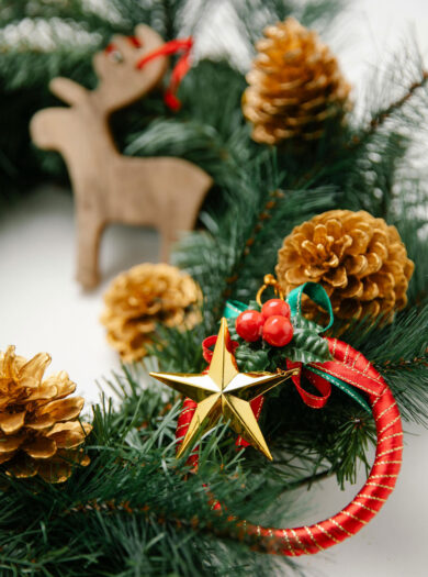 Decorated Christmas wreath with gold pinecones, star ornament, red ribbon and wooden reindeer.