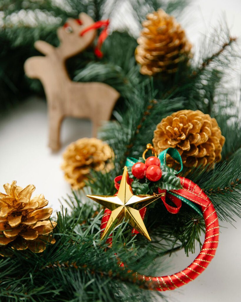 Decorated Christmas wreath with gold pinecones, star ornament, red ribbon and wooden reindeer.