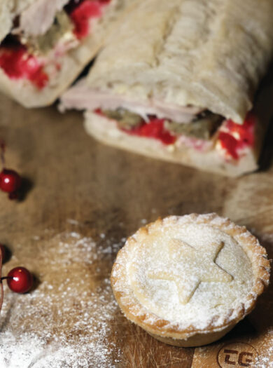 Festive mince pie and turkey sandwich set on a wooden board with christmas berries and icing sugar. ©Gareth Jones