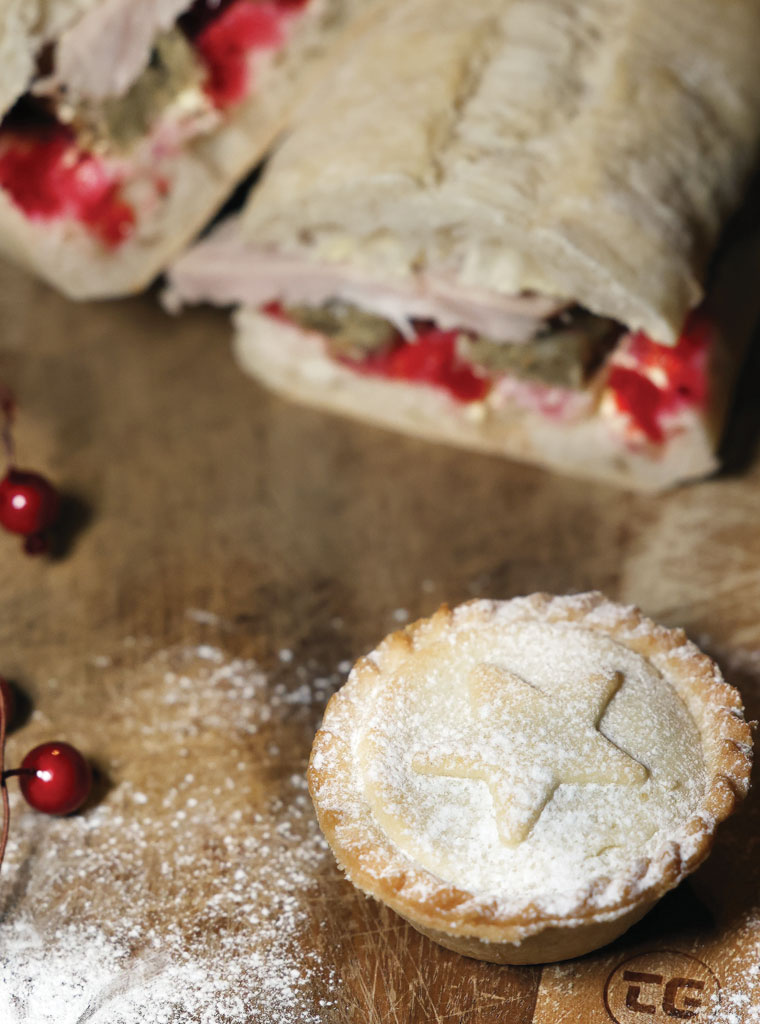 Festive mince pie and turkey sandwich set on a wooden board with christmas berries and icing sugar. ©Gareth Jones